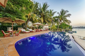 A swimming pool with lounge chairs and umbrellas, surrounded by palm trees and a view of the water. - THE WATERFRONT RESIDENCE (Mombasa)