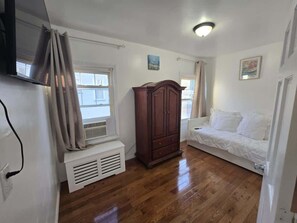 A room with a wooden floor, a white radiator, a wooden wardrobe, a white sofa, and a window with curtains. - Amazing large 3 BD apartment in NJ Close 15 minutes to Metlife (Kearny)