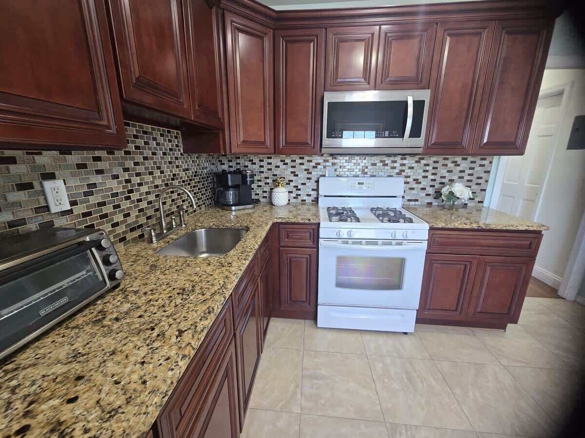 A kitchen with wooden cabinets, a granite countertop, a microwave, a stove, and a toaster.
