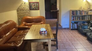 Ein gemütliches Wohnzimmer mit Ledersofa, Holztisch, Bücherregal und einer Küche im Hintergrund.