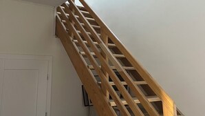 Eine Holztreppe mit Handlauf, eine weiße Tür und ein Kleiderschrank mit gefalteter Kleidung.