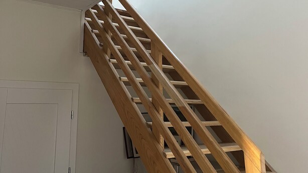 Un escalier en bois avec une rampe, une porte blanche et un placard contenant des vêtements pliés.