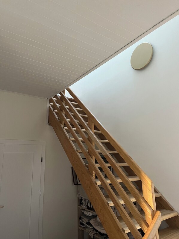 A wooden staircase with a handrail, a white door, and a closet with folded clothes.