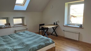Ein Schlafzimmer mit Dachfenster, einem Bett mit gemustertem Überwurf, einem Schreibtisch mit Stuhl und einer Heizung.