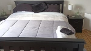 Quarto com cama, mesa de cabeceira, luminária e uma obra de arte na parede.