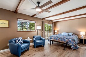 Une chambre à coucher comprenant un lit, deux chaises, une table, un ventilateur de plafond et une fenêtre donnant sur des arbres.
