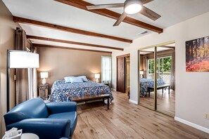 A bedroom with a bed, a desk, a chair, a ceiling fan, and a large mirror.