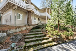 A house with a covered porch, stone steps, and a garden with trees and shrubs.