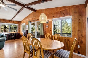 A wooden-paneled room with a round dining table, chairs, and a ceiling fan.