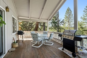 A covered outdoor area with a grill, a table with chairs, and a view of trees.