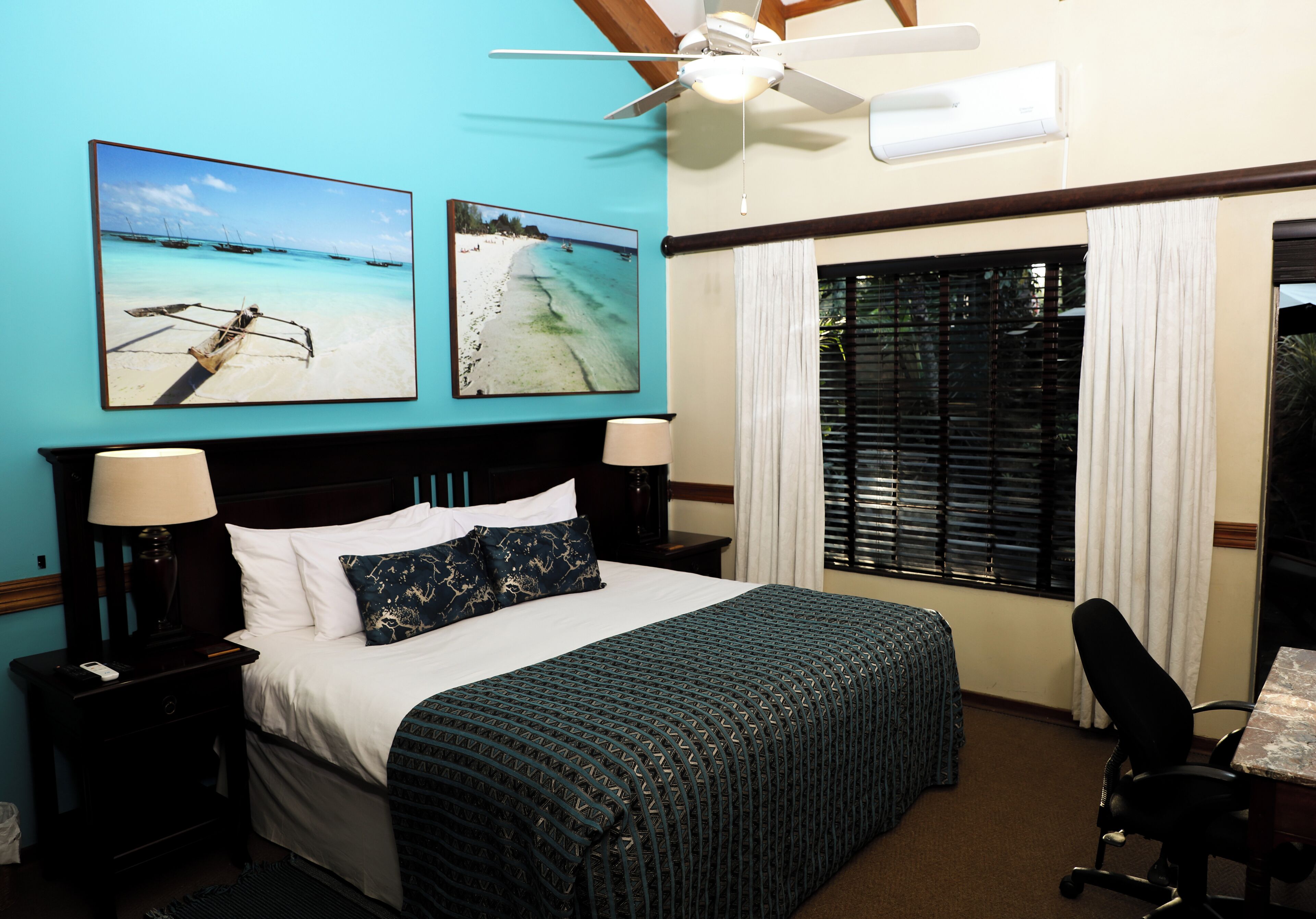A hotel room with a bed, two bedside tables, a desk, and a window with blinds.