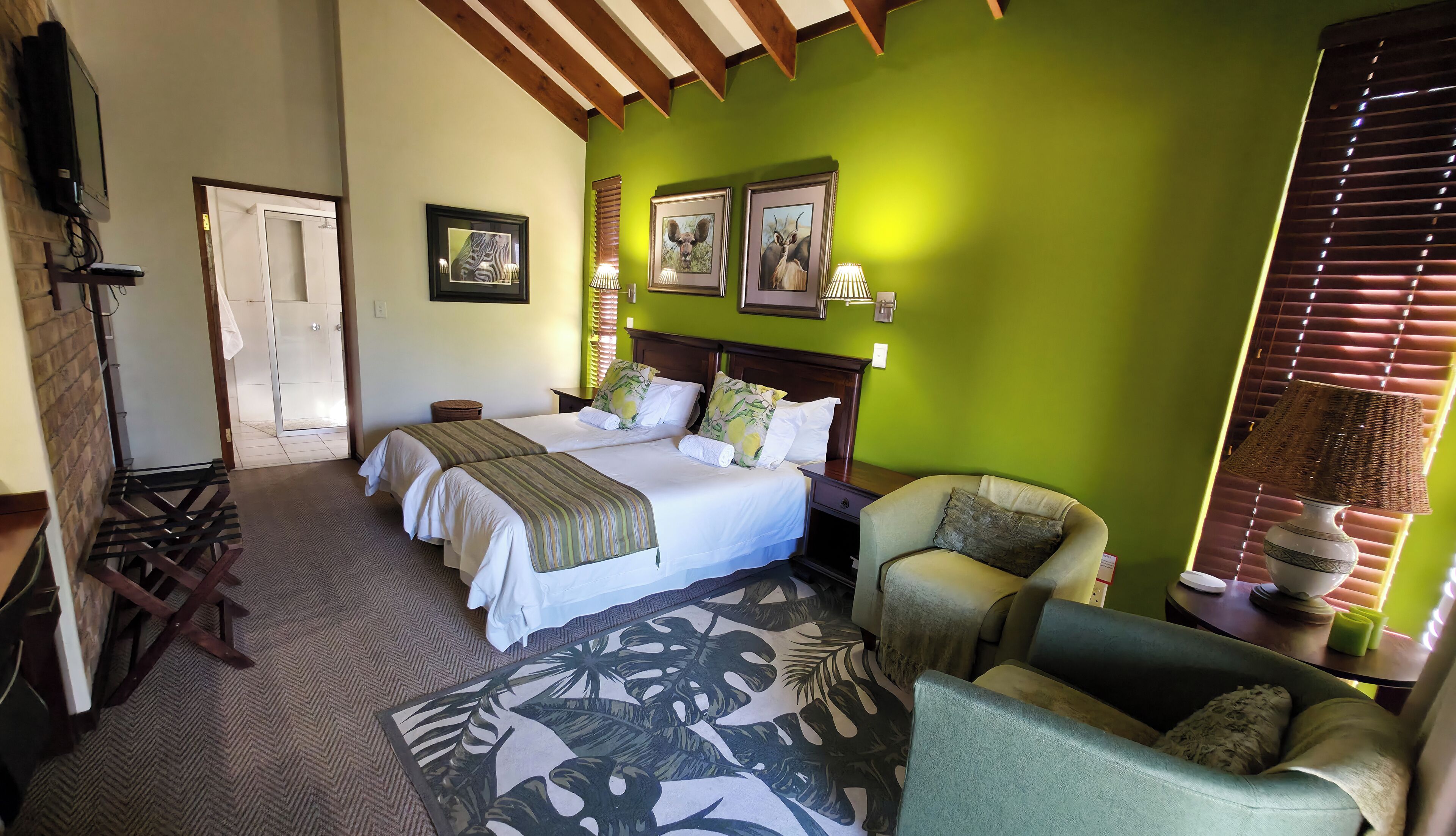 A hotel room with two beds, a chair, a lamp, and a window with blinds.