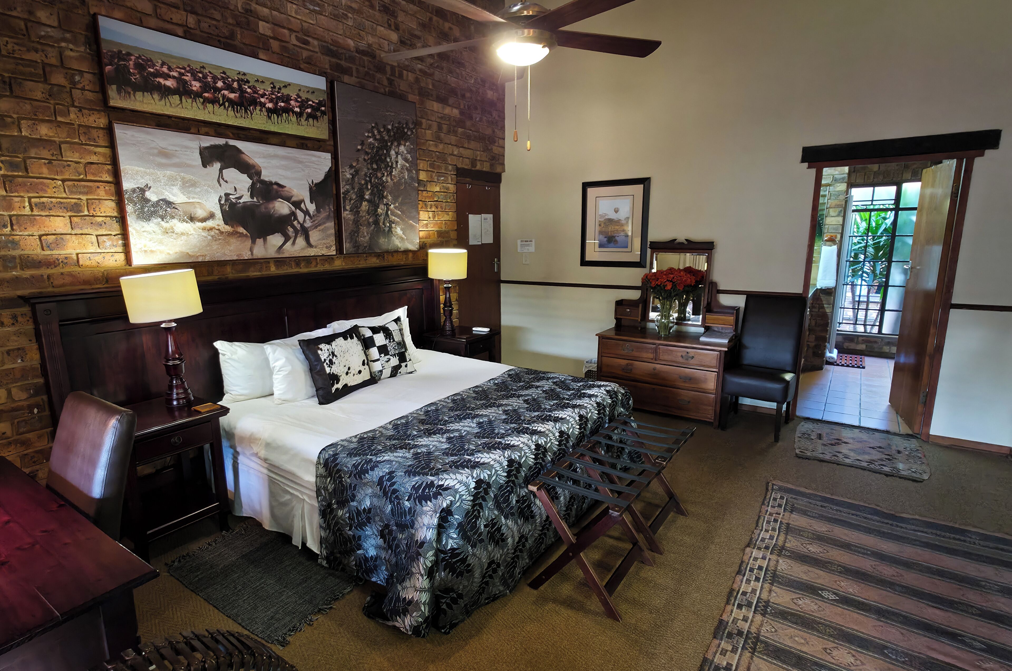 A hotel room with a bed, a desk, a chair, a lamp, a dresser, a mirror, and a door leading to a balcony.