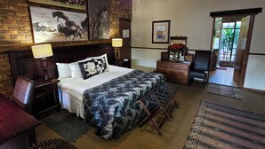 Habitación de hotel con cama, escritorio, silla, lámpara, cómoda, espejo y puerta que da a un balcón.