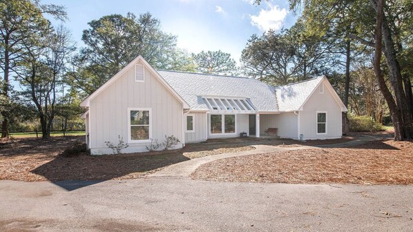 A white single-story house with a sloped roof, a covered porch, and a driveway leading to the entrance.