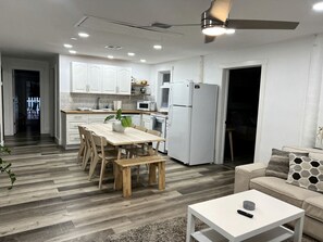 Una cocina moderna con armarios blancos, una mesa de comedor con sillas, un refrigerador blanco y un ventilador de techo.