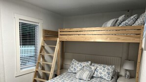 A bunk bed with a ladder, a bedside table with a lamp, and a window with blinds.
