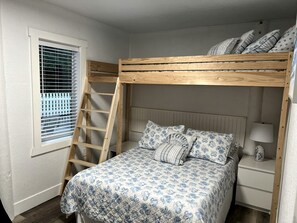 A bunk bed with a ladder, a bedside table with a lamp, and a window with blinds.