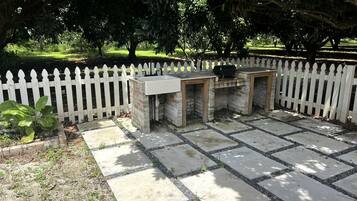 A paved patio with a white picket fence, stone planters, and a brick structure.