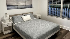 A bedroom with a bed, nightstands, a wall-mounted painting, and a window with blinds.