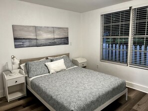 A bedroom with a bed, nightstands, a wall-mounted painting, and a window with blinds.