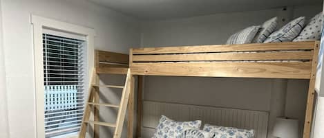 A bunk bed with a ladder, a bedside table with a lamp, and a window with blinds.