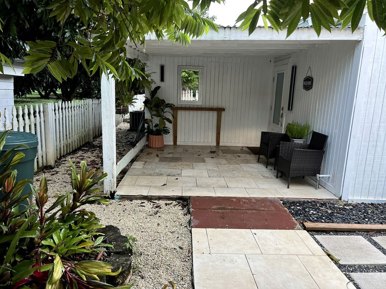 A covered patio area with a white fence, potted plants, and a bench.