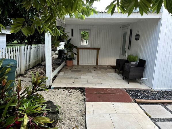 A covered patio area with a white fence, potted plants, and a bench.