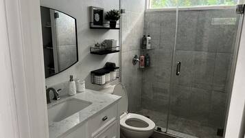 Un baño moderno con cabina de ducha de vidrio, inodoro blanco y lavabo de mármol.