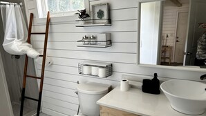 A bathroom with a wooden ladder, white toilet, and a large mirror above a sink with a white basin.