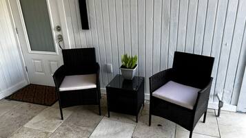 A porch with two wicker chairs, a small table, and a potted plant.