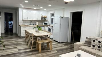 Une cuisine moderne avec des meubles blancs, une table à manger avec des chaises, un réfrigérateur blanc et un ventilateur de plafond.