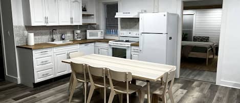 Une cuisine moderne avec des meubles blancs, une table à manger en bois et un réfrigérateur.