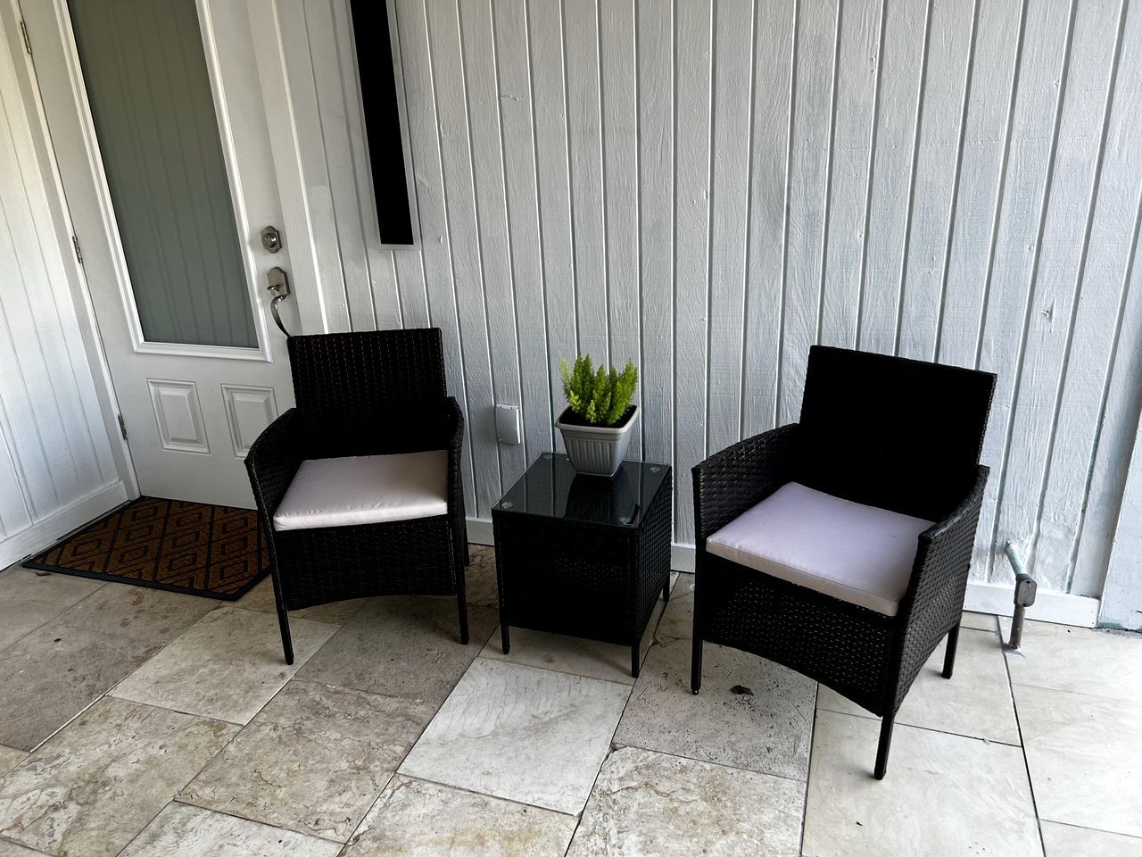 A porch with two wicker chairs, a small table, and a potted plant.