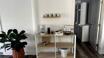 A kitchenette with a coffee station, a potted plant, and a sign indicating a coffee clock.