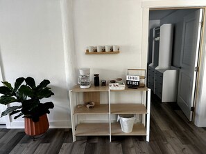 Una kitchenette con estación de café, una planta en maceta y un cartel que indica horario de café.