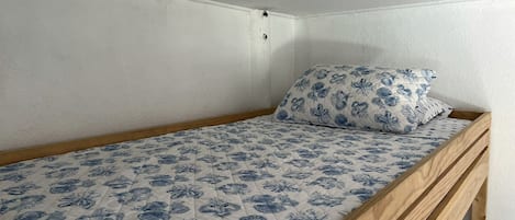 Un lit simple avec une couvre-lit à motifs floraux et un oreiller assorti, dans une chambre d’angle aux murs blancs et au chevet en bois.