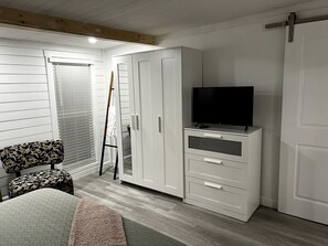 Una habitación con cama, armario, televisor y ventana con persianas.