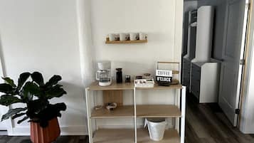 Una kitchenette con estación de café, una planta en maceta y un cartel que indica horario de café.