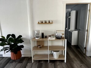 A kitchenette with a coffee station, a potted plant, and a sign indicating a coffee clock.