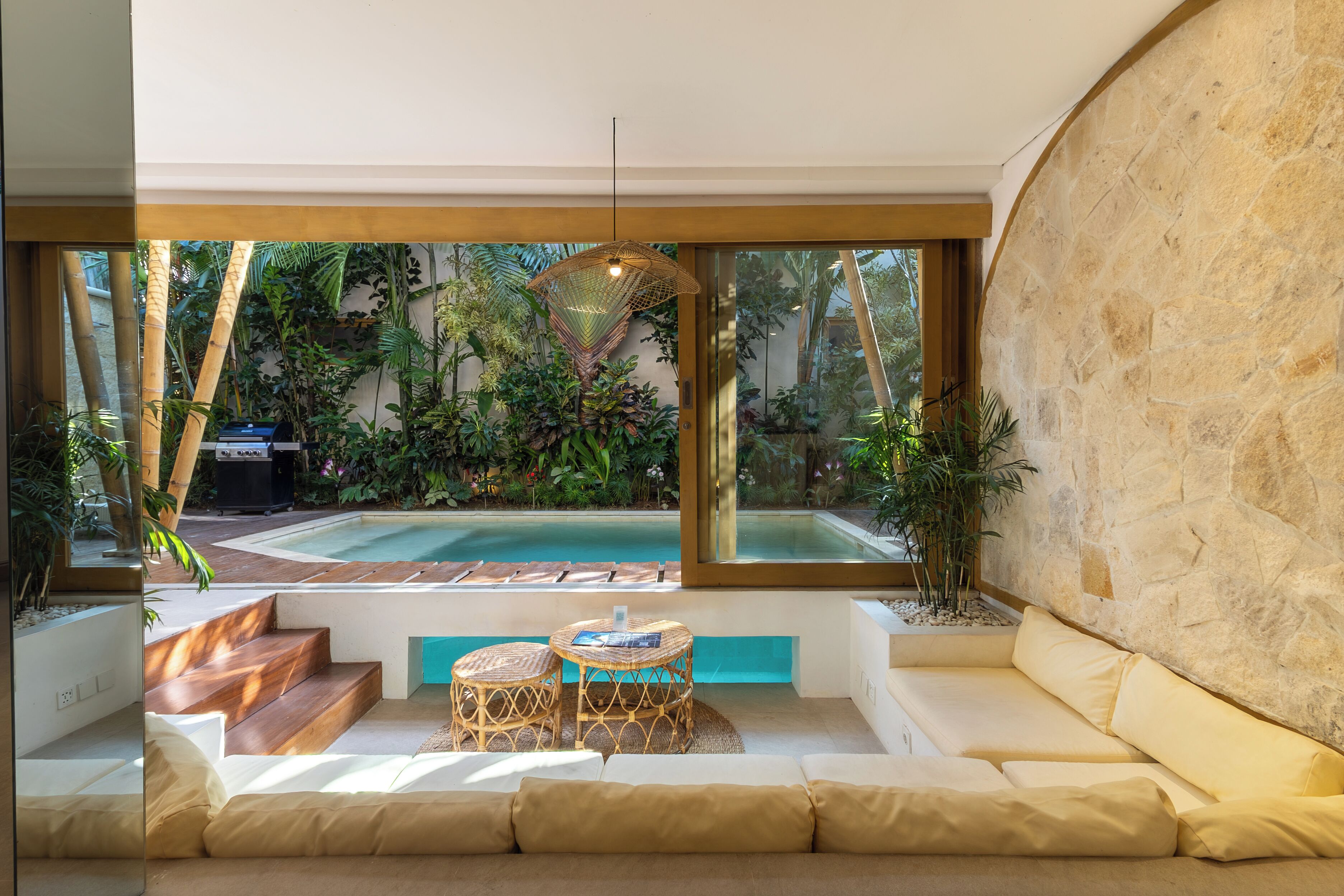 A modern interior with a pool, outdoor seating, and a view of a lush garden.