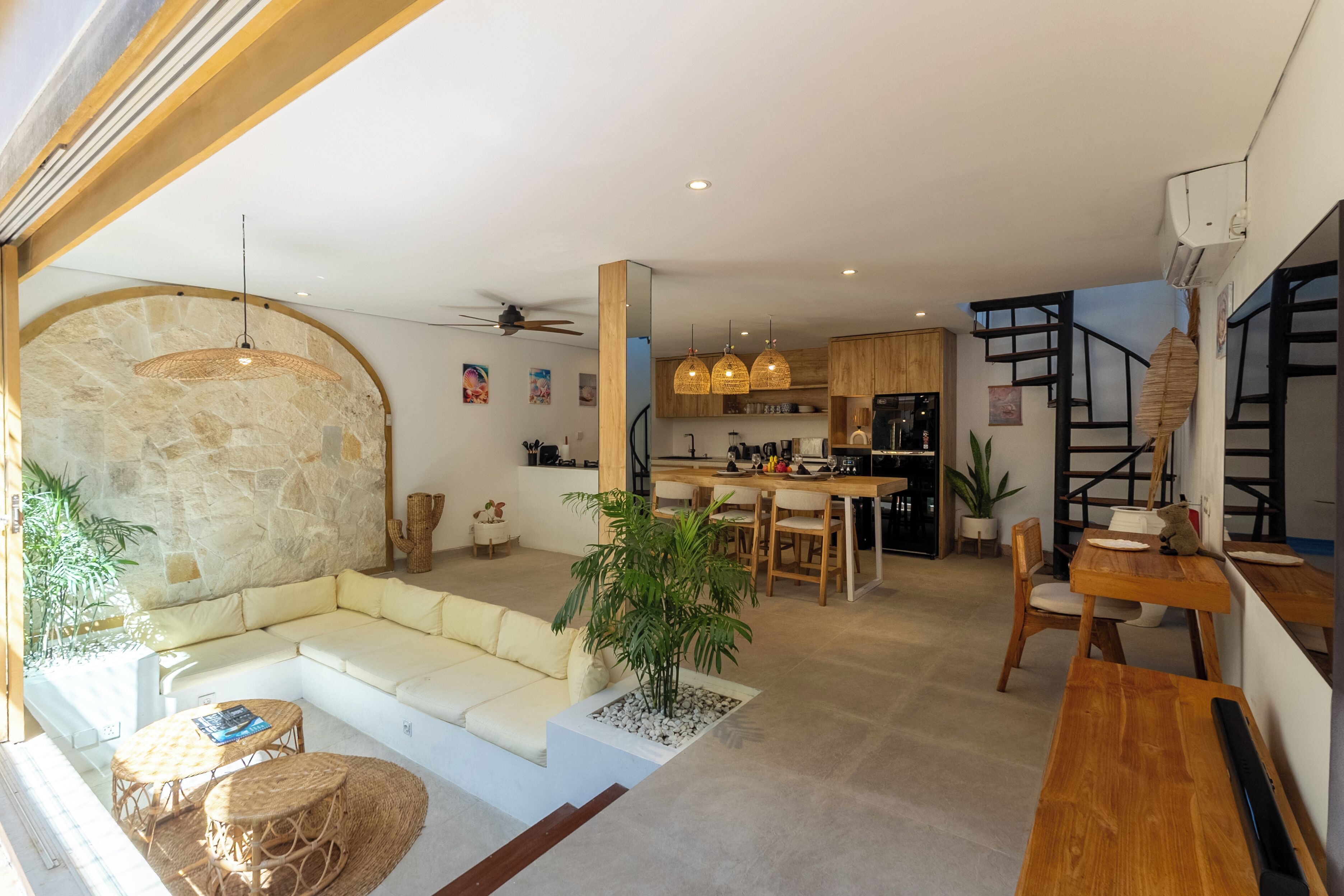 Un interno moderno con una parete decorata in pietra, una zona pranzo, una cucina e un angolo salotto con divano e tavolino.