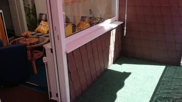 Ein Zimmer mit einer Schiebetür, einem kleinen Tisch mit einer Vase, einem Stuhl und einem Fenster mit Vorhängen.
