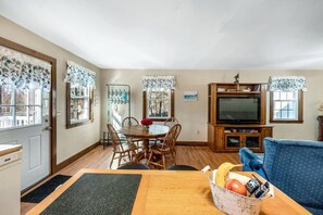 Un comedor con una mesa de madera, sillas y un mueble de televisión con televisor.