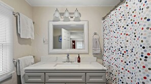 A bathroom with a white vanity, a mirror, three light fixtures, a shower curtain with a polka dot pattern, and a towel rack. - Lakefront Cabin with Spectacular Sunset Views in Colchester, Vermont (Colchester)