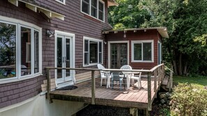 A two-story house with a deck, white chairs, and a small table.