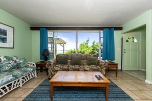 A living room with a sofa, a patterned couch, a coffee table, and a view through large windows.