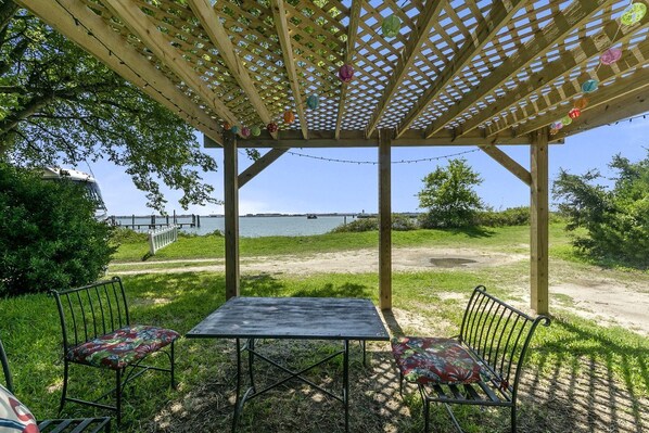 A wooden pergola with a table and chairs, overlooking a body of water.