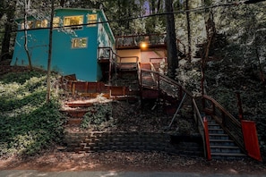 A multi-level wooden structure with a staircase leading to a balcony, surrounded by dense foliage.