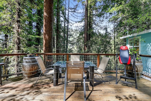 A deck with a table and chairs, surrounded by tall trees.